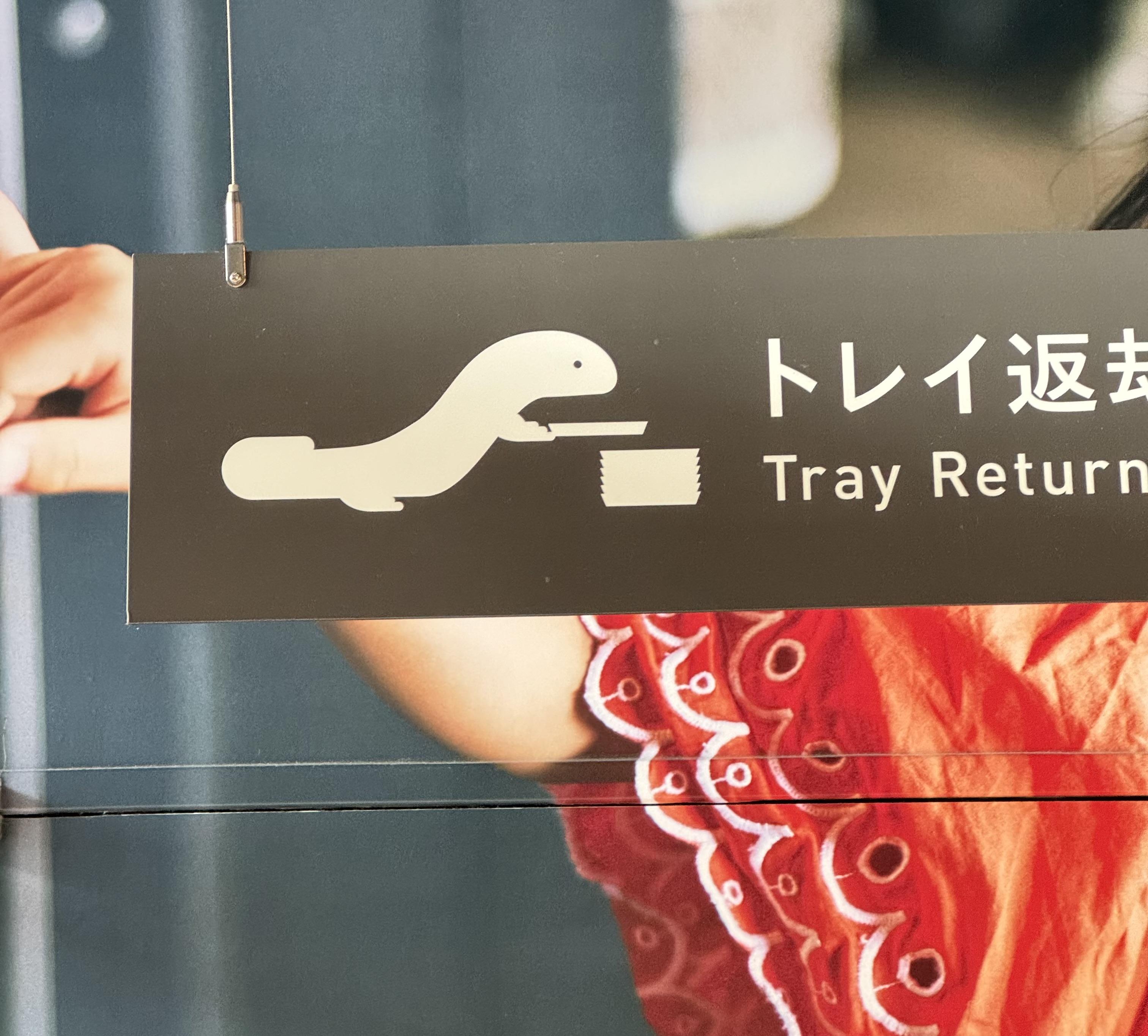 A sign depicting a giant salamander returning a tray at Kyoto Aquarium